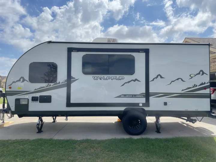 This light gray Wolf Pup Black Label travel trailer, with distinctive mountain graphics, is parked and ready as an rv rental.. Forest River Cherokee Wolf Pup Black Label 2022