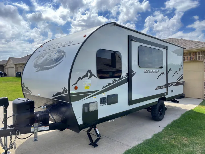 Light-colored Wolf Pup travel trailer with mountain graphics, ready for your next rv rental adventure. Parked on a driveway.. Forest River Cherokee Wolf Pup Black Label 2022