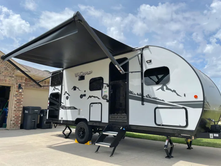 A white Wolf Pup Black Label RV rental is parked with its awning extended, showcasing a ready setup for a camping getaway.. Forest River Cherokee Wolf Pup Black Label 2022