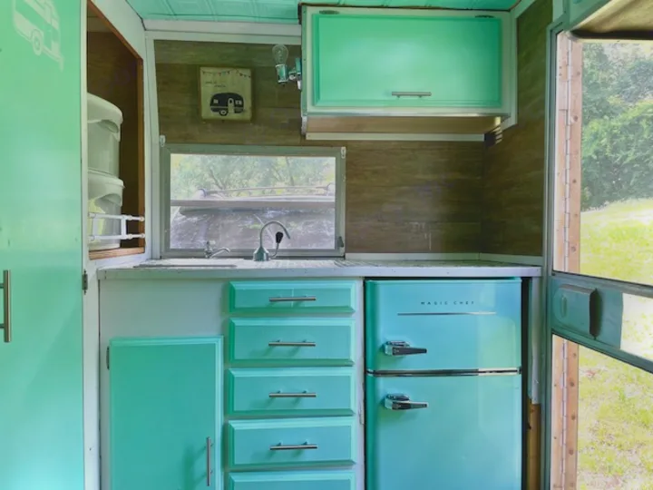 Experience the cozy interior of our turquoise RV rental kitchen, complete with a Magic Chef fridge & scenic window views.. Shasta Compact 1973