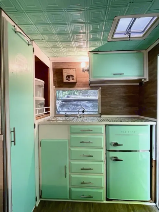 Inside this cute **RV rental**: a mint green & wood retro camper kitchen with fridge & patterned ceiling.. Shasta Compact 1973