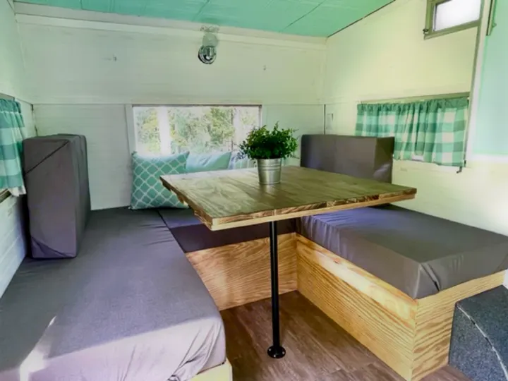 Cozy RV rental interior featuring a built-in dinette with grey cushions, wooden table, and light teal decor.. Shasta Compact 1973