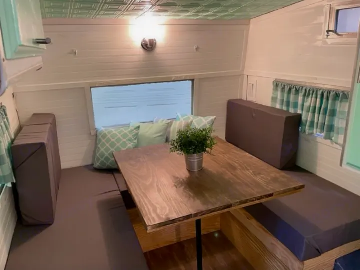 Cozy RV rental interior: a dinette with a wood table, dark cushions, and cheerful checked curtains.. Shasta Compact 1973