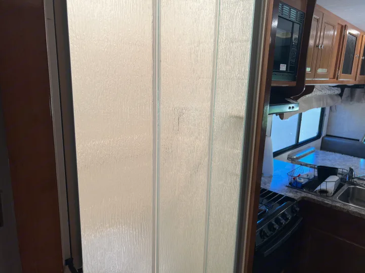RV rental: Textured door for bathroom/shower; beyond, an RV kitchen with microwave, cabinets, stovetop, sink, and dinette.. Coachmen Leprechaun 2019