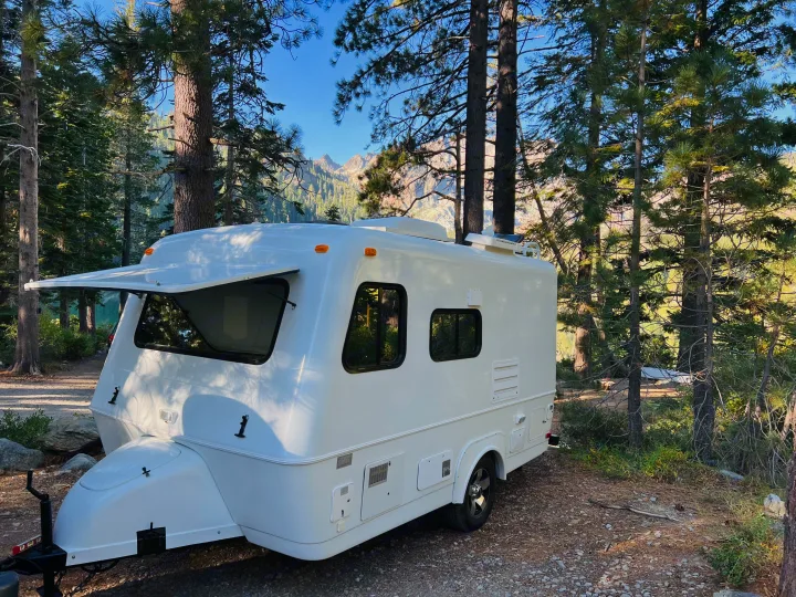 This white RV rental is perfectly situated at a scenic mountain campsite near a lake, ideal for outdoor adventure.. Bigfoot RV Bigfoot RV Trailer 2005