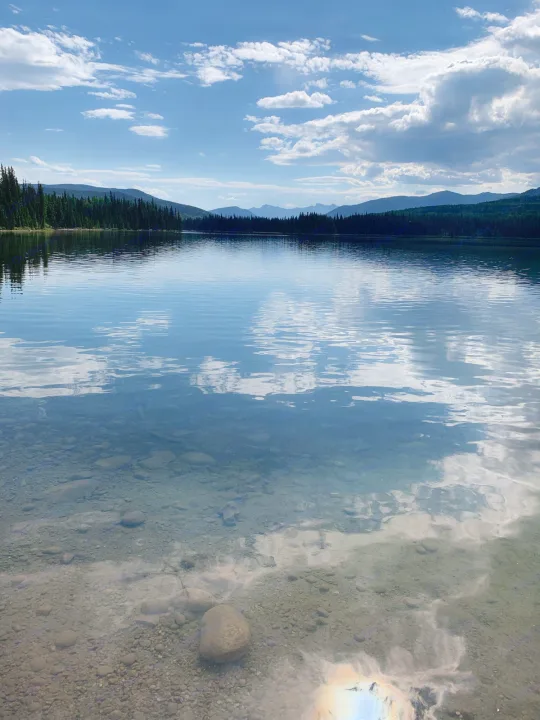 Peaceful lake reflections and clear waters revealing rocks, with forests and mountains beyond – ideal for an RV rental journey.. Starcraft Starflyer 1996