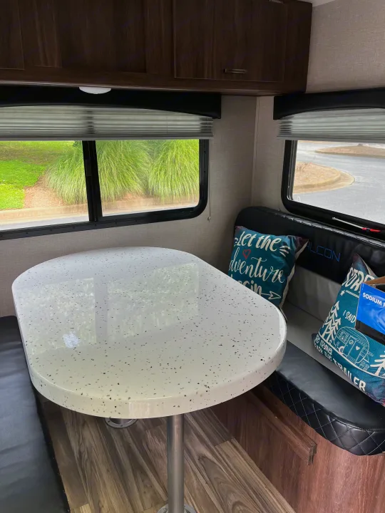 Inviting RV rental dinette with a speckled white table, black bench seating, and windows showing green outdoors.. Travel Lite Falcon 2019