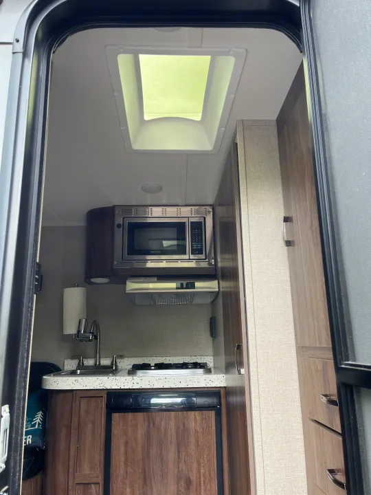 RV rental kitchen: compact galley with microwave, sink, stovetop, and refrigerator. Ideal for road trip cooking & camping.. Travel Lite Falcon 2019