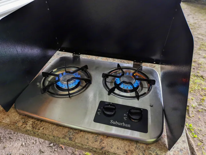 RV rental kitchen: Suburban 2-burner gas stove with blue flames ready for use on a speckled counter.. Keystone RV Springdale 2013