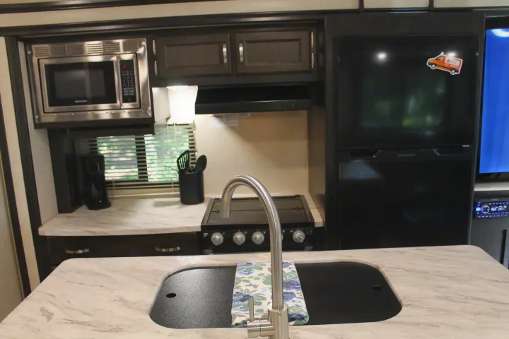 RV rental kitchen: light marble-look counters, sink, microwave, stove, and fridge in a compact layout.. Coachmen Spirit Ultralight 2020