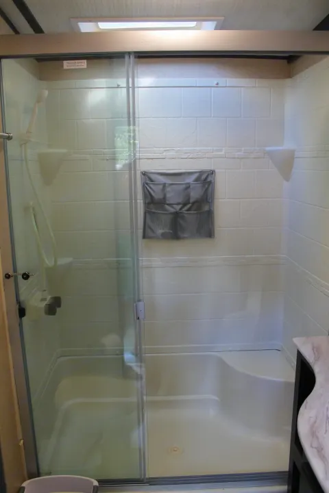 Bright RV rental shower interior features white tiled walls, clear glass sliding door, hand-held shower, and mesh organizer.. Coachmen Spirit Ultralight 2020