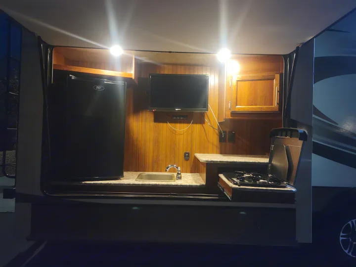 A bright outdoor kitchen in an RV rental, complete with a mini-fridge, sink, stove, and wall-mounted TV for camping trips.. Jayco Eagle 2016