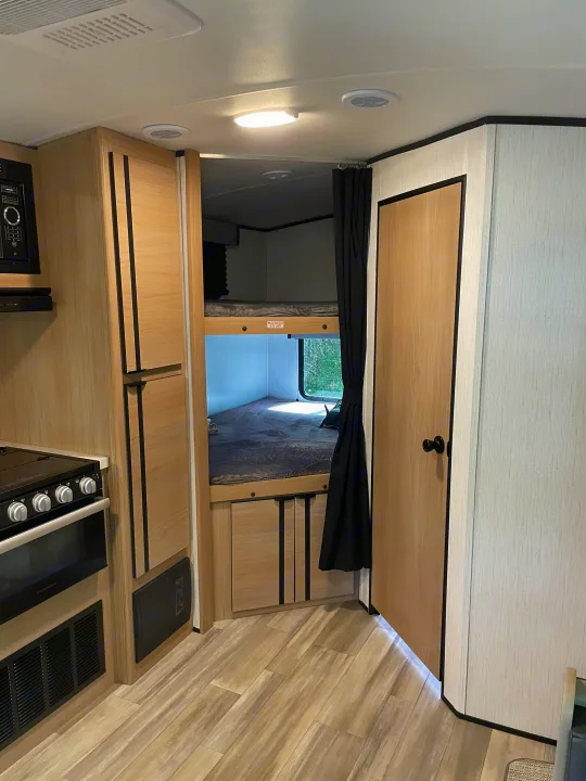 RV rental interior: Kitchen with appliances on the left, next to cozy bunk beds, featuring light wood cabinets and flooring.. Cruiser Rv Corp Radiance 2022
