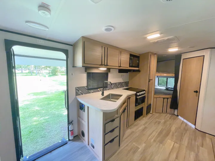 Bright rv rental interior featuring a modern kitchen with sink, stove, and microwave, plus bunk beds and exit to a green lawn.. Cruiser Rv Corp Radiance 2022