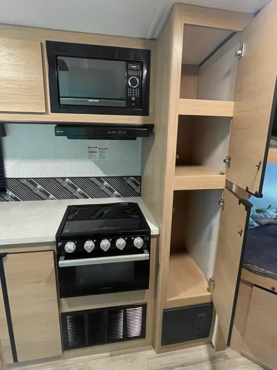 This RV rental kitchen features a GreyStone microwave, gas range/oven, and spacious pantry storage for compact cooking needs.. Cruiser Rv Corp Radiance 2022