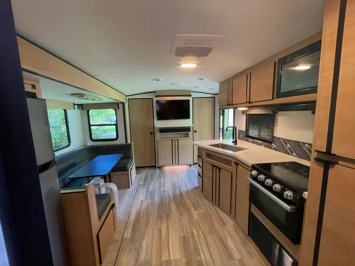 Spacious RV rental interior with a bright kitchen, dining booth, and entertainment center with TV. Features light wood cabinetry and flooring.. Cruiser Rv Corp Radiance 2022