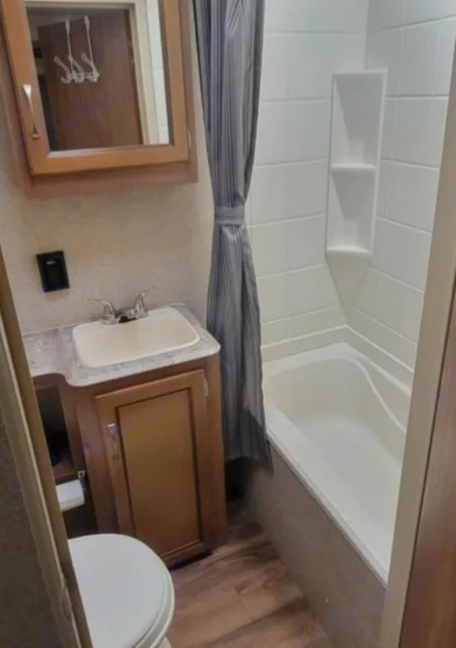 This compact RV rental bathroom includes a vanity with sink, a toilet, and a bathtub/shower combo with a shower curtain.. Coachmen Catalina 2019