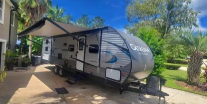 Ready for adventure: a gray Catalina travel trailer RV rental with awning extended, parked by a house.. Coachmen Catalina 2019