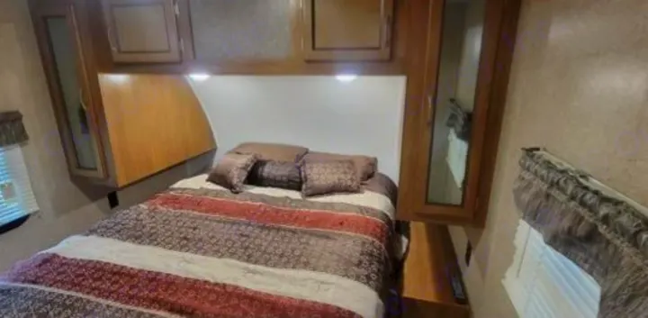 RV rental interior: A cozy bedroom featuring a patterned bed, overhead lights, and built-in wood cabinets for comfortable travel.. Coachmen Catalina 2019