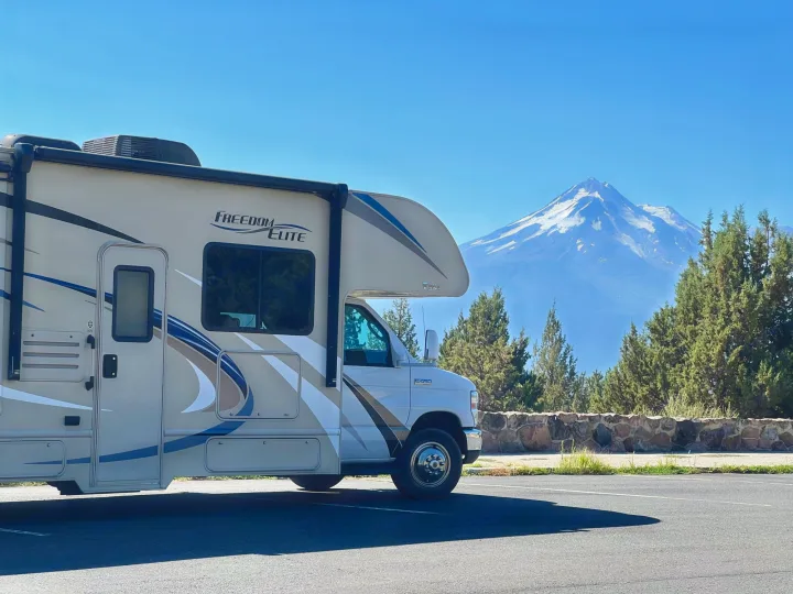 A Freedom Elite RV rental is parked in a sunny lot, overlooking a majestic snow-capped mountain vista, ideal for scenic travel adventures.. Thor Freedom Elite 2019