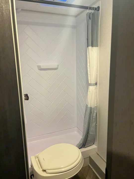 Compact rv rental bathroom featuring a white shower stall with herringbone pattern, toilet, and striped shower curtain.. Forest River Salem FSX 2022
