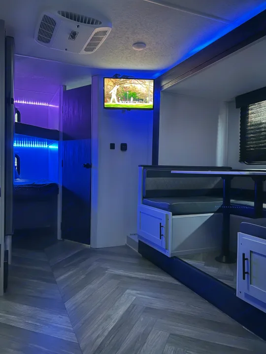 Blue-lit RV rental interior featuring a modern dinette, TV, and comfortable bunk beds.. Forest River Salem FSX 2022