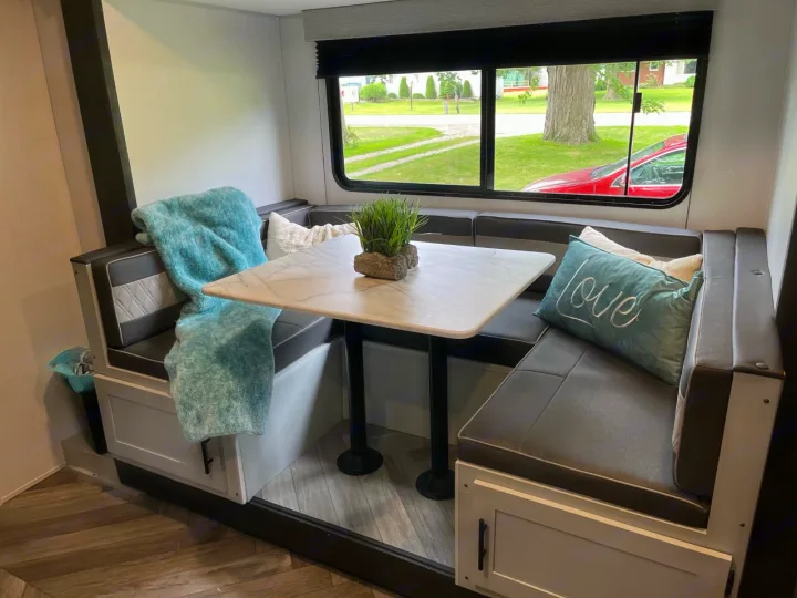 Inside an **RV rental**: a modern dinette with dark seating, a marble-look table, and a view of nature. Comfy and ready for travel!. Forest River Wildwood FSX Plantium 2022