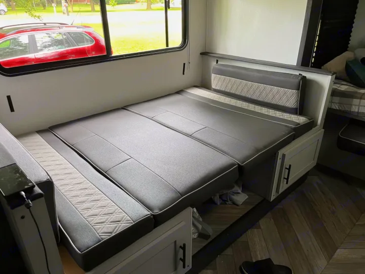 RV rental: Dinette converted to a comfy bed with grey cushions & quilted accents, beside a window view.. Forest River Wildwood FSX Plantium 2022