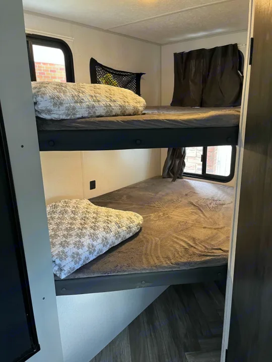A bright RV rental interior featuring two comfortable bunk beds with grey bedding and windows, perfect for family sleeping.. Forest River Wildwood FSX Plantium 2022