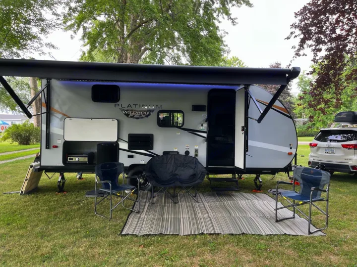 Enjoying the outdoors with a grey rv rental travel trailer set up for camping, featuring an awning, chairs, and outdoor kitchen.. Forest River Wildwood FSX Plantium 2022