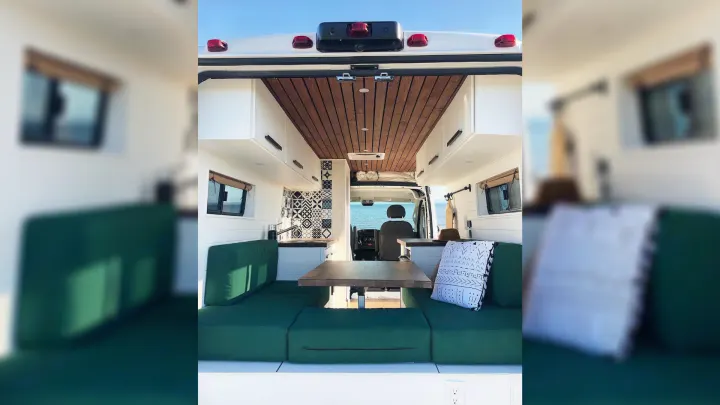 Spacious rv rental interior with green cushions, wooden table, and ocean view. Perfect for van life adventures.. RAM Promaster 2500 2017