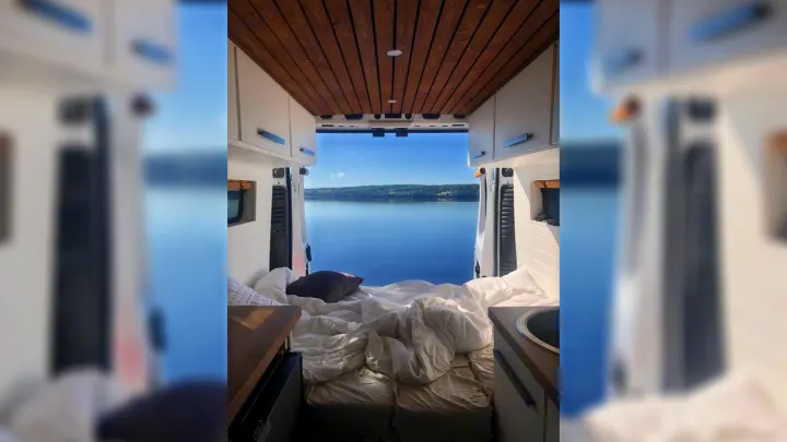 Inside a comfortable RV rental, featuring a bed, kitchen area, and panoramic lake view out the back doors. Ideal for travel.. RAM Promaster 2500 2017