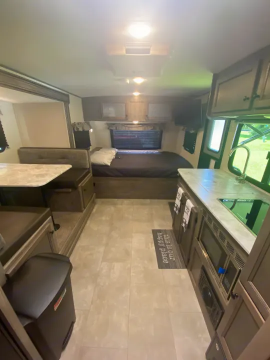 View of a modern rv rental interior with a cozy bed, dinette seating, and compact kitchen area.. Coachmen Apex Nano 2021