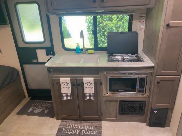 Well-equipped RV rental kitchen features sink, stove, microwave, cabinets, and scenic window views for your journey.. Coachmen Apex Nano 2021