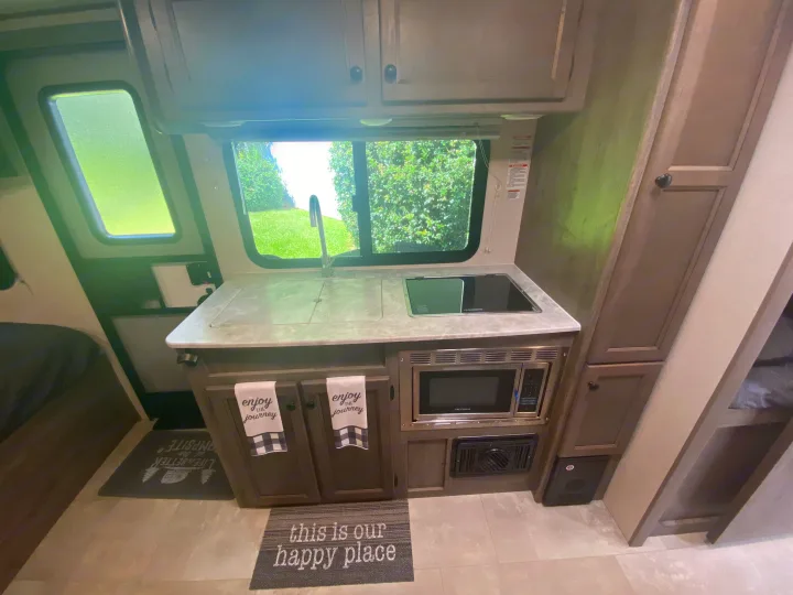 RV rental interior featuring a compact kitchen with a sink, stovetop, microwave, and cozy decorative touches.. Coachmen Apex Nano 2021