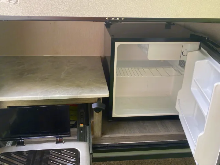 RV rental outdoor kitchen featuring an open mini-fridge, a stone-look countertop, and a pull-out stove/grill.. Coachmen Apex Nano 2021