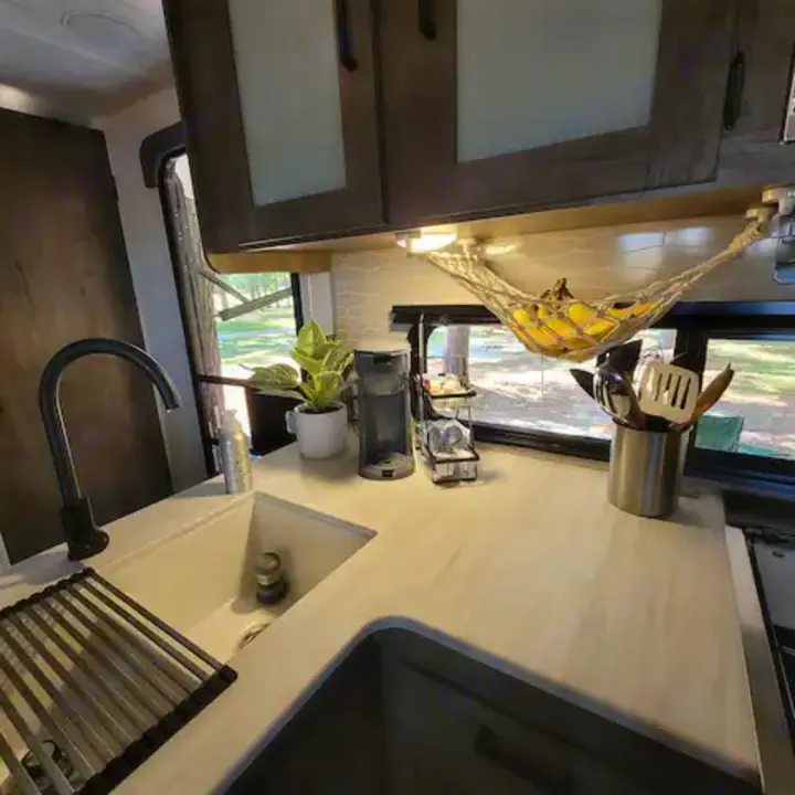 RV rental kitchen showing sink, coffee maker, fruit hammock, and utensils. Enjoy amenities and outdoor views on your mobile adventure.. Forest River Salem Cruise Lite 2022