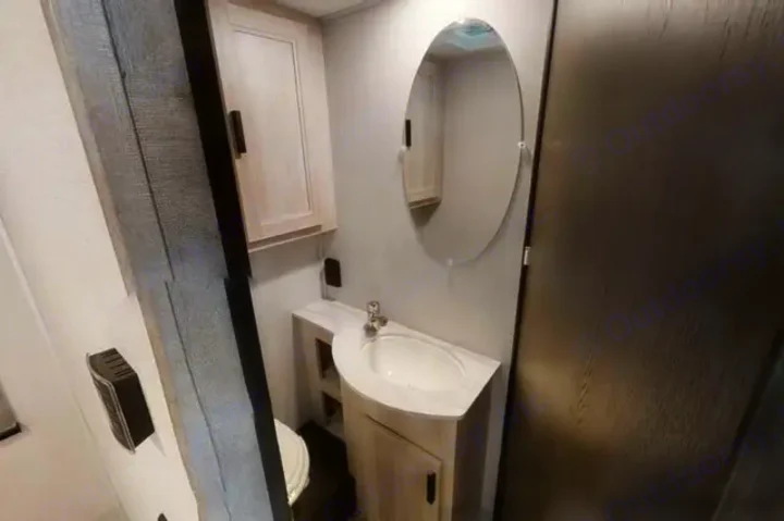 This RV rental's compact bathroom features a light wood vanity with a white sink, an oval mirror, and a toilet.. Forest River Sunseeker LE 2021