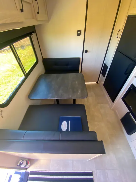 RV rental interior featuring a bright dinette with black benches, a gray table, a window, and overhead storage.. Coachmen Apex 2021