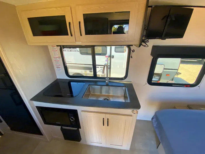 This RV rental's interior features a compact kitchen with a sink, cooktop, microwave, cabinets, TV, and sleeping area.. Coachmen Apex 2021