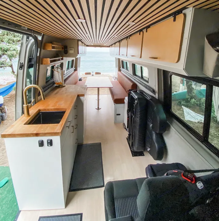 Stunning RV rental: interior of a modern camper van with kitchen, dining area, slatted ceiling, and ocean view.. Mercedes Sprinter 2021