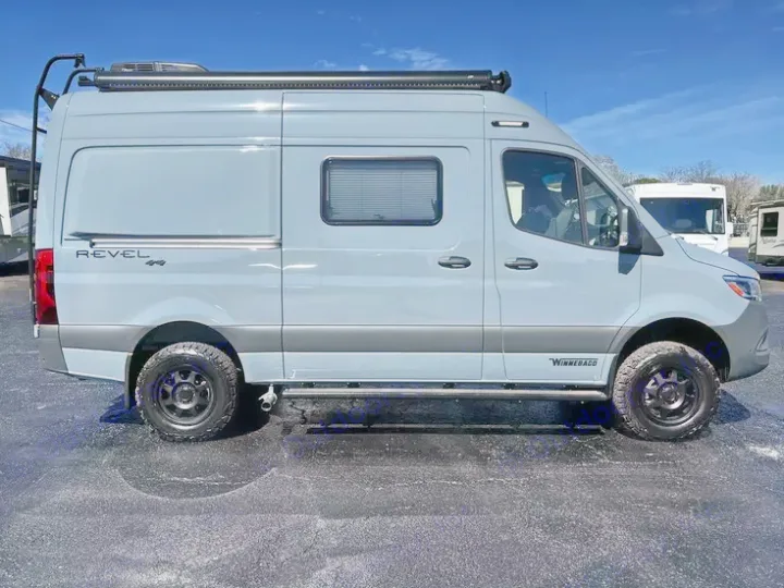 Side view of a light blue Winnebago Revel 4x4 adventure van, excellent for rv rental adventures. Note the rear ladder and roof awning.. Winnebago Revel 2022