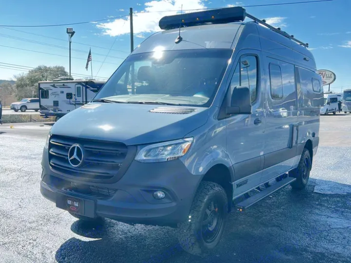 Adventure awaits! This customized grey Mercedes Sprinter **rv rental** van features off-road tires & roof rack, parked outdoors.. Winnebago Revel 2022