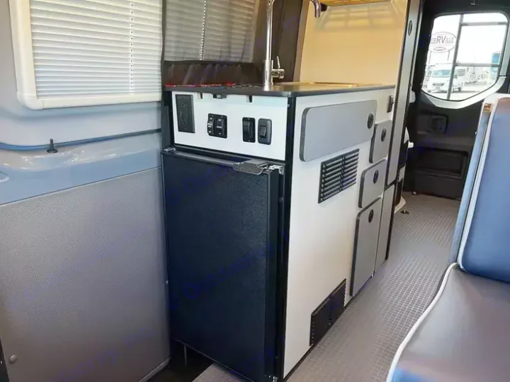 Compact RV rental interior featuring a functional kitchen with sink, refrigerator, and controls, ideal for camper van adventures.. Winnebago Revel 2022