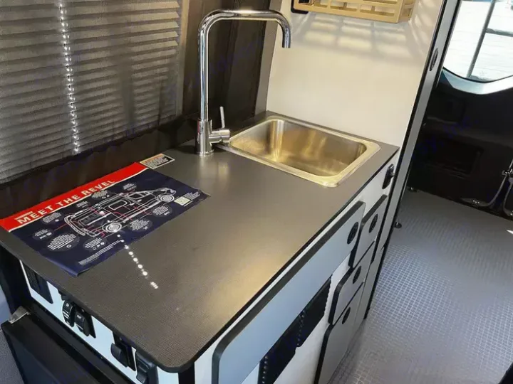 RV rental interior: a compact kitchen with stainless steel sink, chrome faucet, and dark gray counter.. Winnebago Revel 2022