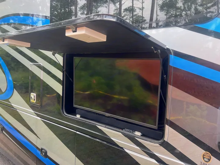 RV rental outdoor entertainment: an open compartment reveals a TV and soundbar on the side of this striped recreational vehicle.. Thor Outlaw 2022