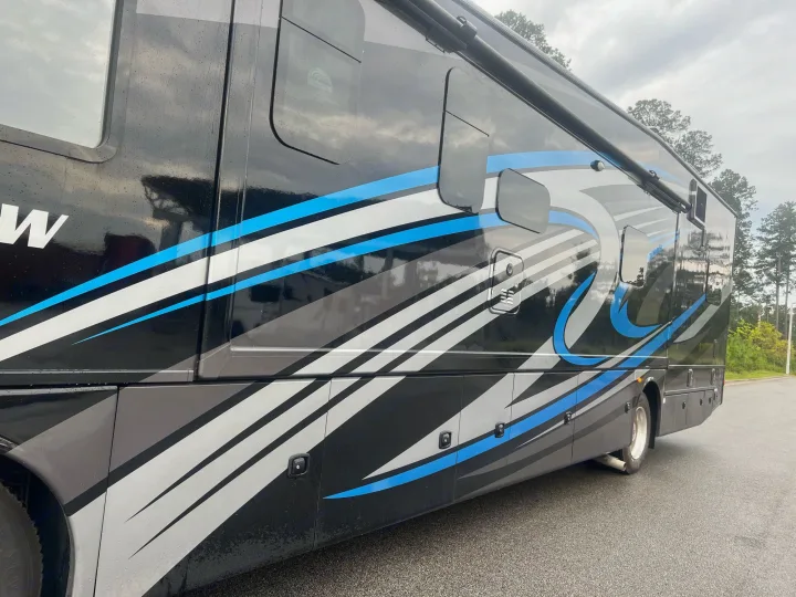 Side view of a sleek black RV with blue, white, and gray graphics, perfect for an rv rental getaway.. Thor Outlaw 2022