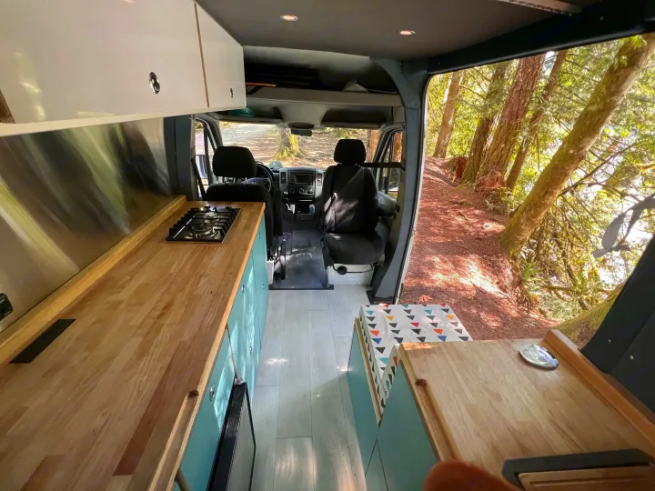 Inside an **rv rental** camper, a modern kitchen meets a wild forest view. Perfect for nature adventures & cozy living.. Mercedes Sprinter 2016
