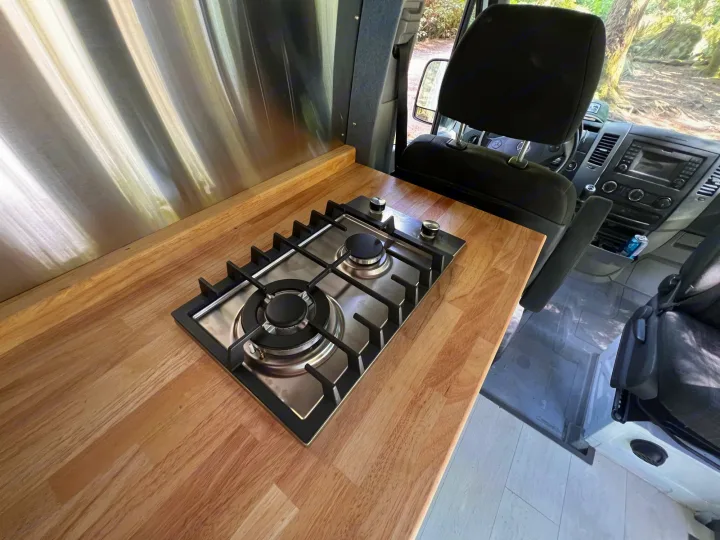 RV rental interior showcasing a modern kitchen with wooden counters, a built-in gas stove, and stainless steel backsplash.. Mercedes Sprinter 2016