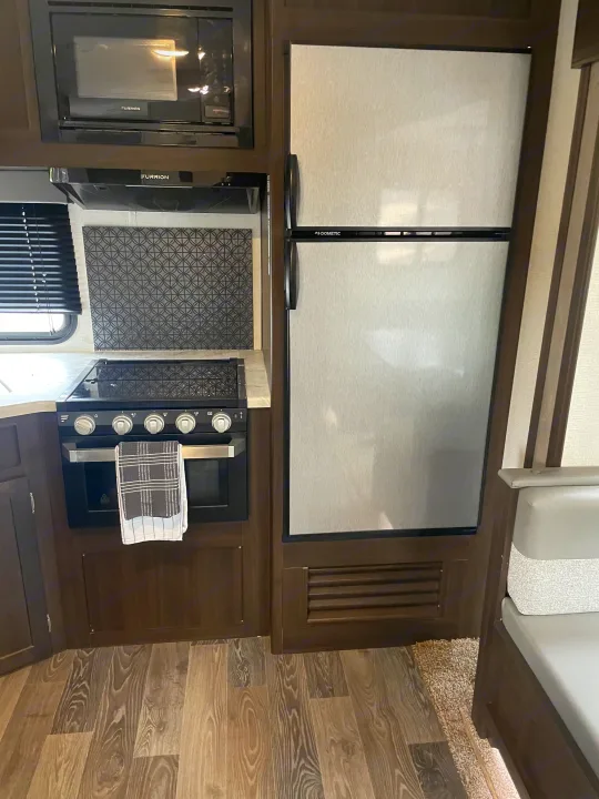 RV rental kitchen showing a Furrion microwave & range hood, Dometic refrigerator, and stove with oven, featuring modern wood-look flooring.. Keystone RV Springdale 2020